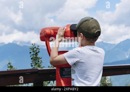 ragazzo che osserva il panorama delle montagne attraverso un binocolo fisso. Foto di alta qualità Foto Stock