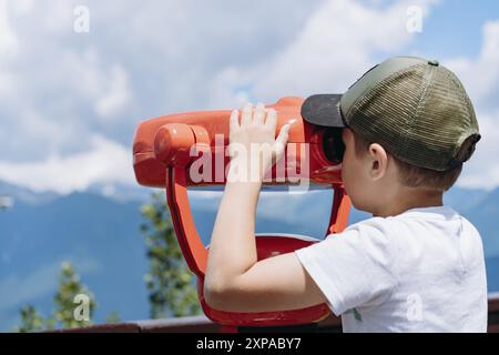 ragazzo che osserva il panorama delle montagne attraverso un binocolo fisso. Foto di alta qualità Foto Stock