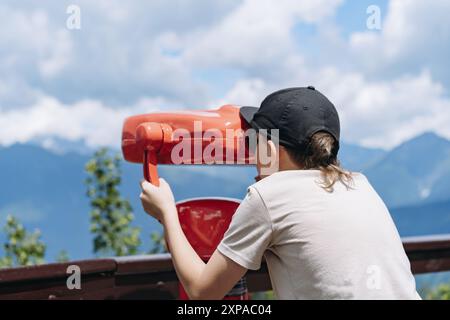 ragazzo che osserva il panorama delle montagne attraverso un binocolo fisso. Foto di alta qualità Foto Stock