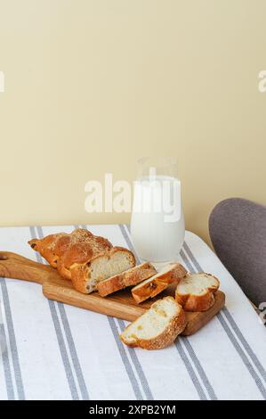 affettare il pane fatto in casa su una tavola di legno e latte in un bicchiere Foto Stock