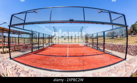 Padel Tennis su superficie rossa astro con campo recintato in vetro in campagna in una giornata di cielo blu. Foto Stock