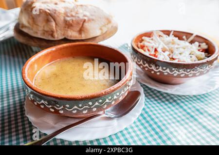 Goditi una tradizionale zuppa balcanica, con tenero maiale e cavolo in un brodo cremoso, servito con pane croccante su un tavolo di legno, un delizioso sapore Foto Stock