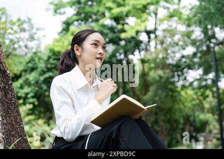 Giovane donna professionale che lavora all'aperto con notebook in mano, concetto aziendale, natura, ambiente di lavoro produttivo Foto Stock