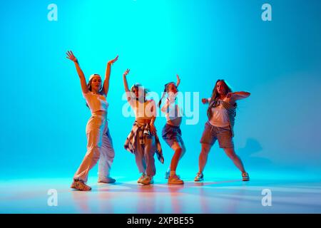 Ritratto di gruppo di ballerini che eseguono movimenti contemporanei in movimento con una vibrante luce al neon su sfondo blu sfumato in studio. Foto Stock