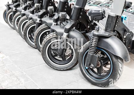 Gli scooter parcheggiavano ordinatamente in fila su un marciapiede della città. Fila di scooter elettrici a noleggio neri allineati su una strada Foto Stock