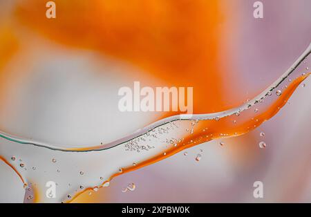 Immagine astratta con un liquido arancione che scorre con gocce d'acqua sospese su uno sfondo morbido. Foto Stock
