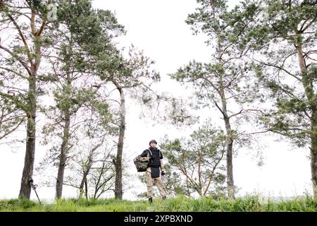 Il giovane soldato in uniformi e gilet tattico lavora nella foresta e si prepara all'azione in una base forestale temporanea. Un uomo fa nel lavoro di sminamento Foto Stock