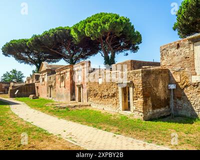 Edifici funerari di una o due piani quadrati, spesso circondati da un recinto; soffitti a botte o tetti piatti; facciate in mattoni adornate con timpani triangolari, plinti, lesbiche, colonne e capitelli; piccole finestre e porte incorniciate da soglie in travertino, stipiti ed epistoli. La necropoli si sviluppò ai lati della via Flavia tra la fine del i e il IV secolo d.C. - Necropoli di Portus nell'Isola Sacra, Fiumicino, Roma, Italia Foto Stock