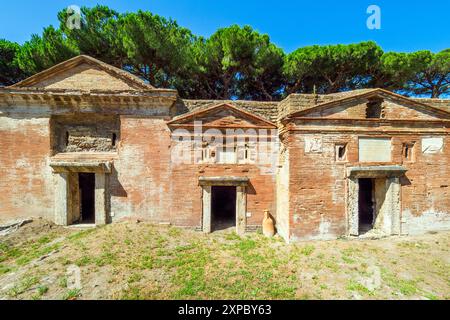 Edifici funerari di una o due piani quadrati, spesso circondati da un recinto; soffitti a botte o tetti piatti; facciate in mattoni adornate con timpani triangolari, plinti, lesbiche, colonne e capitelli; piccole finestre e porte incorniciate da soglie in travertino, stipiti ed epistoli. La necropoli si sviluppò ai lati della via Flavia tra la fine del i e il IV secolo d.C. - Necropoli di Portus nell'Isola Sacra, Fiumicino, Roma, Italia Foto Stock