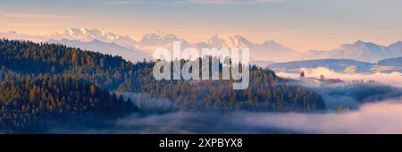 Un'ampia immagine panoramica 3:1 di una mattina d'estate nebbiosa all'alba nell'Emmental, una valle della Svizzera centrale, nel cantone di Berna, con una vi Foto Stock