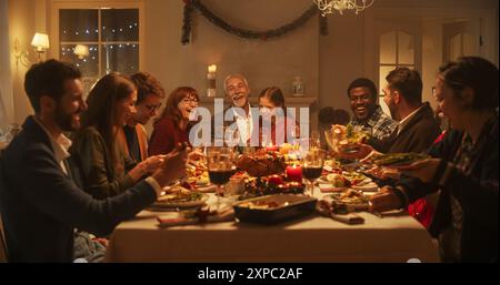 I membri della famiglia multigenerazionale condividono storie divertenti e gioia durante una cena di tacchino di Natale. I genitori felici e i bambini cantano canti natalizi insieme, ballano dietro un tavolo e scintillano Foto Stock