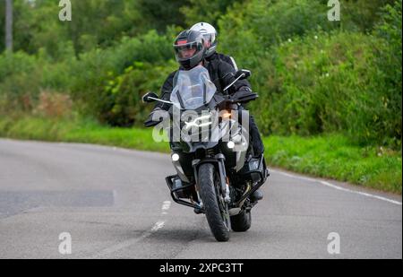 Whittlebury, Norhants, Regno Unito - 4 agosto 2024. Uomo e passeggero gobbo in sella a una motocicletta BMW R1250 GS te su una strada di campagna britannica Foto Stock