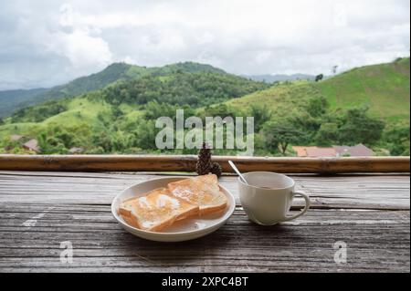 Colazione con pane tostato con cioccolata calda in tazza su un bancone in legno, con vista sulle montagne al mattino Foto Stock