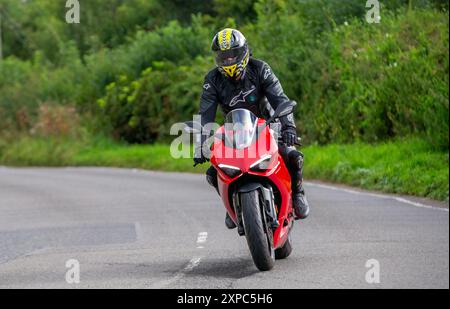 Whittlebury, Norhants, Regno Unito - 4 agosto 2024. Uomo che guida una Ducati Panigale V2 rossa del 2021 su una strada di campagna britannica Foto Stock