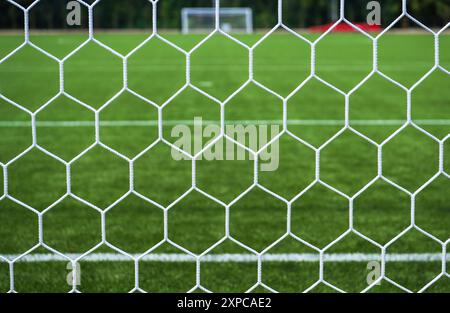 Vista ravvicinata di una rete da calcio con un lussureggiante campo di erba verde e pali di porta visibili sullo sfondo. Foto Stock
