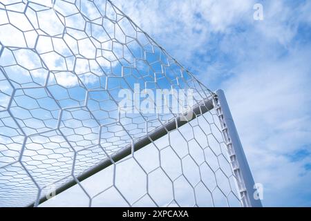 Primo piano di una rete da calcio bianca con un cielo blu vivace sullo sfondo, che mette in risalto i dettagli della struttura rispetto all'ambiente naturale. Foto Stock