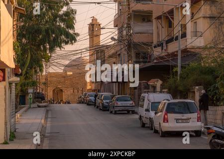 La strada che va al minareto della moschea a Tiro, il sud del Libano con auto parcheggiate ed edifici del Medio Oriente. Foto Stock