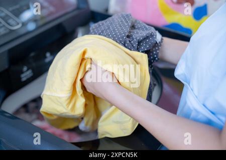 Una giovane donna sta mettendo i vestiti in una lavatrice Foto Stock