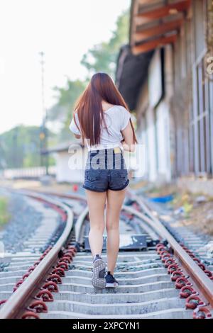 Soft and Smooth Focus, Una giovane donna asiatica cammina da sola lungo i binari della ferrovia verso la sua destinazione desiderata. La parte posteriore di una giovane donna che cammina Foto Stock