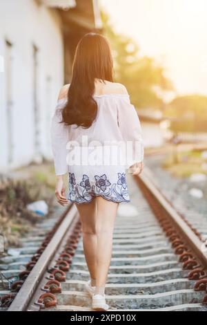 Soft and Smooth Focus, Una giovane donna asiatica cammina da sola lungo i binari della ferrovia verso la sua destinazione desiderata. La parte posteriore di una giovane donna che cammina Foto Stock