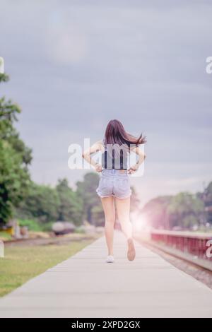 Soft and Smooth Focus, Una giovane donna asiatica cammina da sola lungo i binari della ferrovia verso la sua destinazione desiderata. La parte posteriore di una giovane donna che cammina Foto Stock