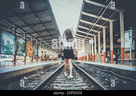 Soft and Smooth Focus, Una giovane donna asiatica cammina da sola lungo i binari della ferrovia verso la sua destinazione desiderata. La parte posteriore di una giovane donna che cammina Foto Stock