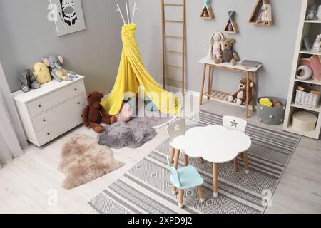 Elegante interno della camera per bambini con tavolo, sedie, giocattoli e tenda da gioco Foto Stock