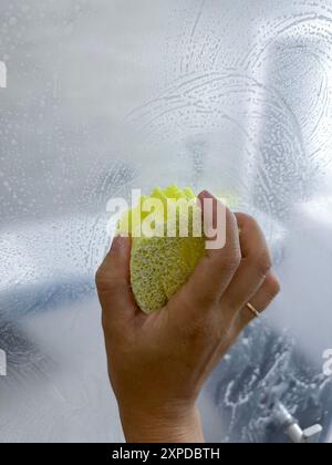 donne che puliscono a mano il vetro della doccia con spugna gialla . Foto di alta qualità Foto Stock