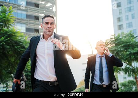 Due uomini d'affari di successo, vestiti in tuta, che corrono perché sono in ritardo per una riunione di lavoro. I lavoratori aziendali si affrettano a raggiungere la loro azienda. I dipendenti esecutivi si recano sul posto di lavoro. Foto di alta qualità Foto Stock