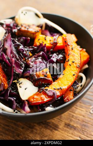 Verdure invernali saltate con cavolo rosso, zucca invernale e tempeh sui tagliatelle. Guarnite con zenzero sottaceto e semi di sesamo nero. Foto Stock