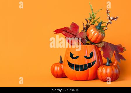 Tazza a forma di zucca di Halloween malvagia, foglie autunnali, zucche e con spazio per testo su sfondo arancione. Sfondo del concetto di Halloween Foto Stock