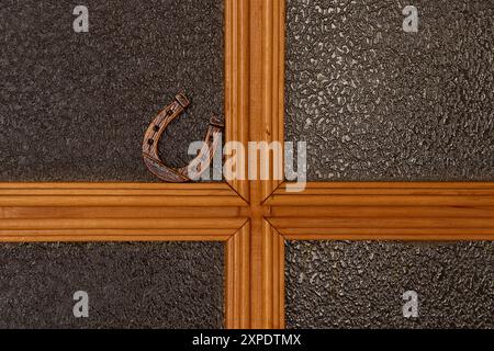 Un piccolo ferro di cavallo di legno si erge su una porta interna di vetro in un appartamento, un simbolo di buona fortuna Foto Stock