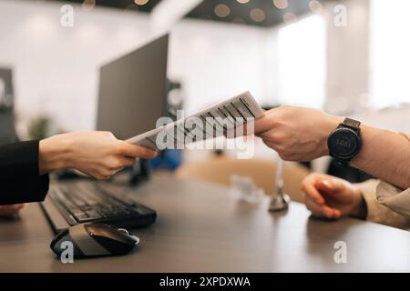 Primo piano di un manager e di un cliente irriconoscibile che scambiano documenti seduti alla scrivania in ufficio. Manager donna che consegna il contratto da leggere e. Foto Stock