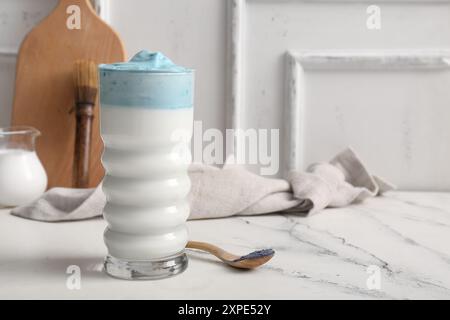 Bicchiere di latte Matcha dalgona blu e cucchiaio di legno con matcha in polvere sul tavolo Foto Stock