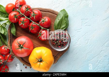 Pomodori a bordo con pepe e rametto di basilico su sfondo azzurro. Primo piano Foto Stock