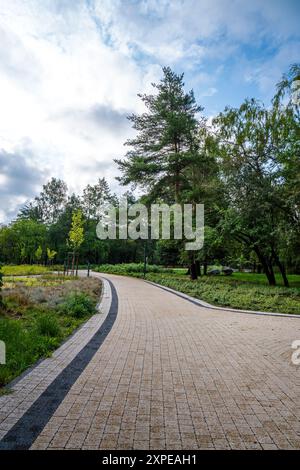 Percorso tortuoso attraverso il lussureggiante Green Park circondato da alti alberi sotto il cielo nuvoloso Foto Stock