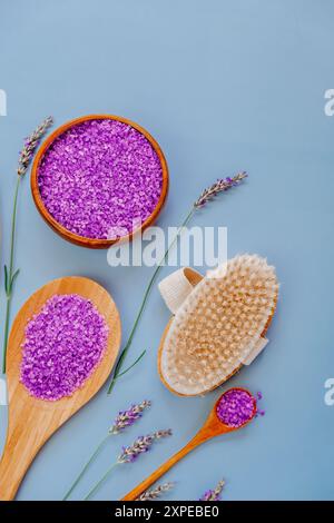 Sale viola in tazze e cucchiai di legno, pennelli a setole e fiori di lavanda sono disposti in modo ordinato su uno sfondo viola. Estratto di lavanda Foto Stock