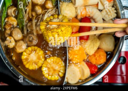 Una persona sta mangiando cibo da una grande pentola di cibo. Il cibo include carne, verdure e frutti di mare Foto Stock