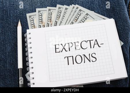 Iscrizione aspettative parola su un quaderno a scacchi in una composizione con banconote in dollari e una matita Foto Stock