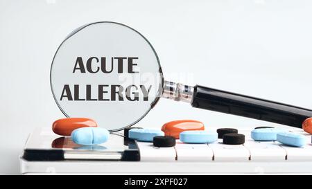 Medicina e concetto di salute. Testo ALLERGIA ACUTA tramite una lente di ingrandimento su una calcolatrice con tavolette su sfondo grigio. Il concetto di medicina Foto Stock