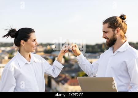 Coppia che scambia le chiavi della casa sul tetto con vista sulla città Foto Stock