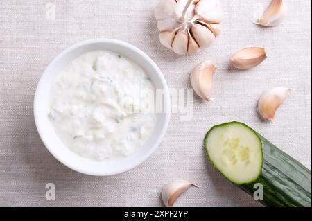 Tzatziki fresco in una ciotola bianca su tessuto di lino. Salsa rinfrescante, zuppa o salsa, fatta di yogurt affaticato salato, mescolato con cetrioli, aglio ed erbe aromatiche. Foto Stock