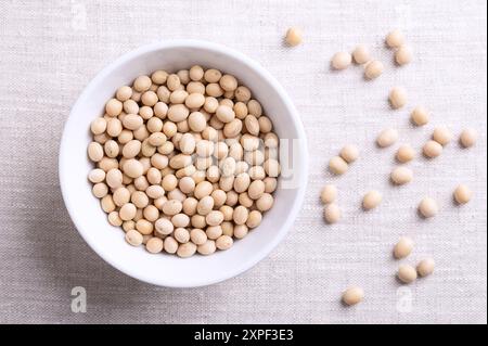 Semi di soia secchi, semi di soia o soia in un recipiente bianco su tessuto di lino. Semi interi e grezzi della leguminosa e dei semi oleosi Glycine max. Foto Stock