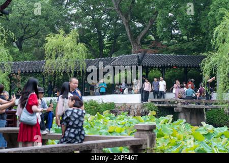 Suzhou, Cina - 11 giugno 2024: Un gruppo di persone si siede vicino a un ponte in un tradizionale giardino cinese affacciato su uno stagno pieno di l Foto Stock