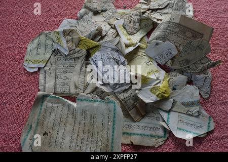 Terengganu, Malesia - 23 agosto 2024 : primo piano pezzi di versi del Corano danneggiati a causa del contatto con l'acqua su sfondo rosso Foto Stock