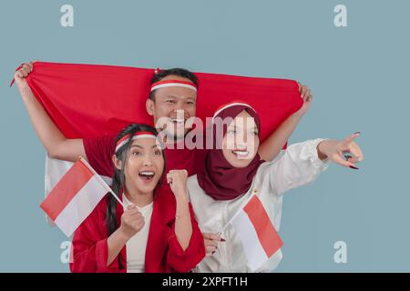 Tre indonesiani stanno sorridendo la loro bandiera e puntando a qualcosa. Indonesia Independence Day Concept. Foto Stock