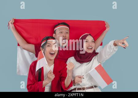 Tre indonesiani stanno tenendo la bandiera del paese che indica qualcosa e alzano il pugno per festeggiare. Indonesia Independence Day Concept. Foto Stock