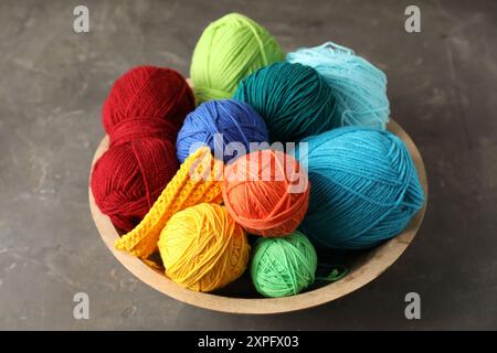 Diversi filati e campioni di maglia in una ciotola su un tavolo a trama grigia Foto Stock