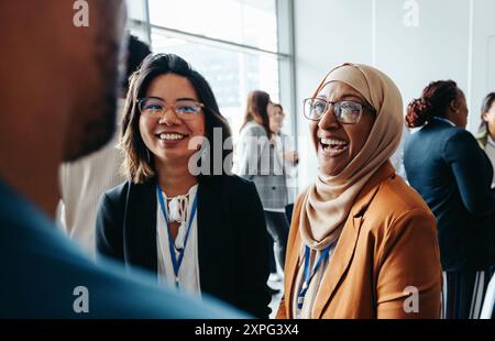 Colleghi donne che interagiscono in un workshop aziendale, condividono sorrisi felici e si impegnano in conversazioni vivaci, promuovendo il lavoro di squadra e il networking Foto Stock