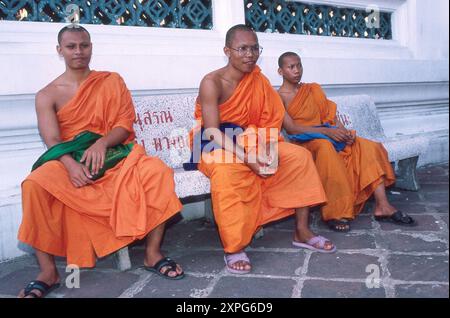 3 monaci buddisti seduti su una panchina di pietra nel Tempio di Wat po, Bangkok, Thailandia Foto Stock